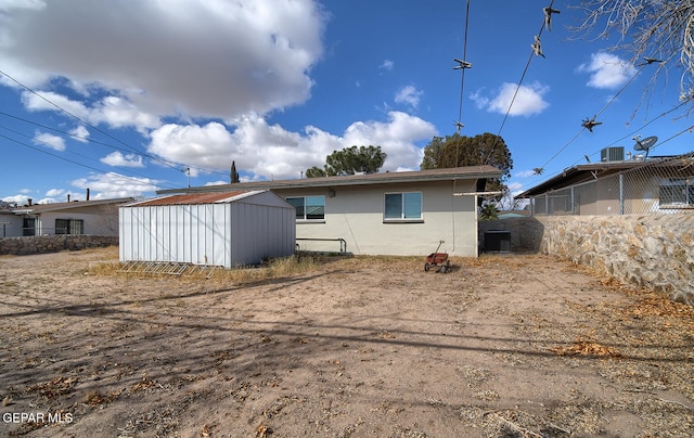 rear view of house with central AC unit and a shed