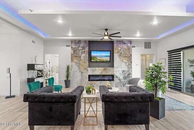 living room with ceiling fan, light hardwood / wood-style floors, a raised ceiling, and a premium fireplace