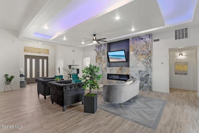 living room with ceiling fan, light hardwood / wood-style flooring, a raised ceiling, and a tiled fireplace