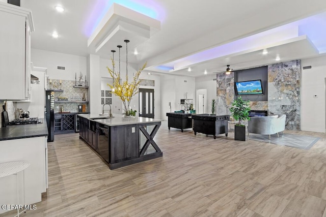 kitchen featuring a fireplace, white cabinetry, dark brown cabinets, sink, and an island with sink