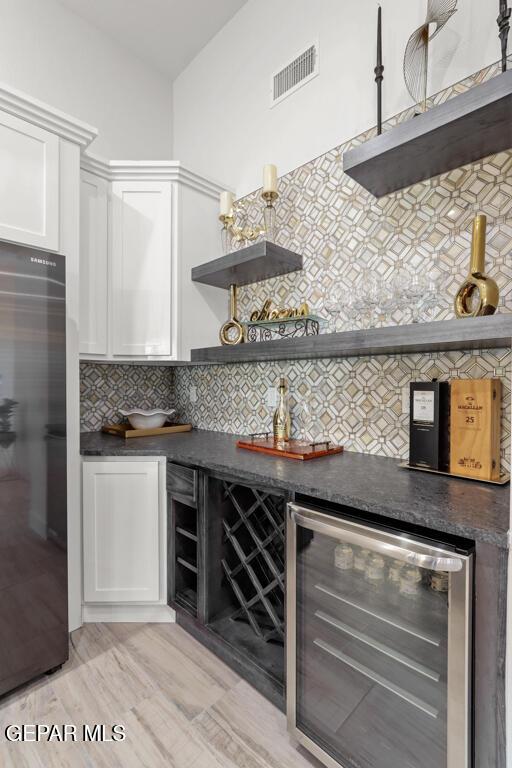 bar featuring white cabinetry, wine cooler, decorative backsplash, stainless steel refrigerator, and light hardwood / wood-style flooring