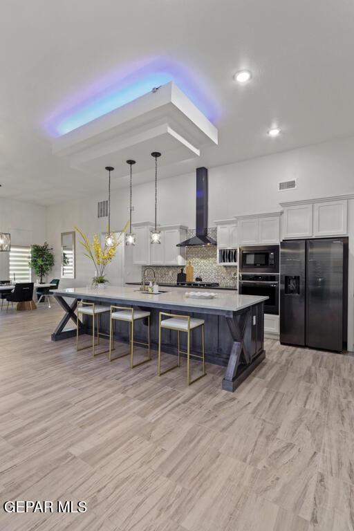kitchen featuring wall chimney exhaust hood, white cabinetry, pendant lighting, and appliances with stainless steel finishes