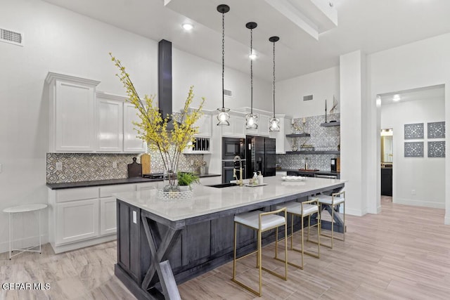 kitchen featuring black appliances, white cabinetry, hanging light fixtures, a kitchen island with sink, and a kitchen breakfast bar