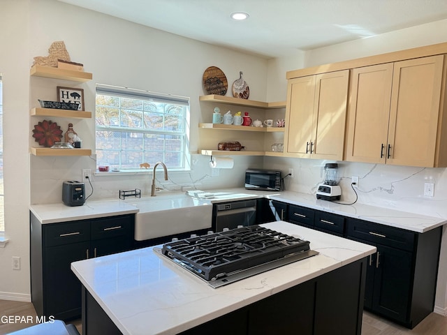 kitchen with light brown cabinetry, sink, light stone counters, a center island, and black appliances