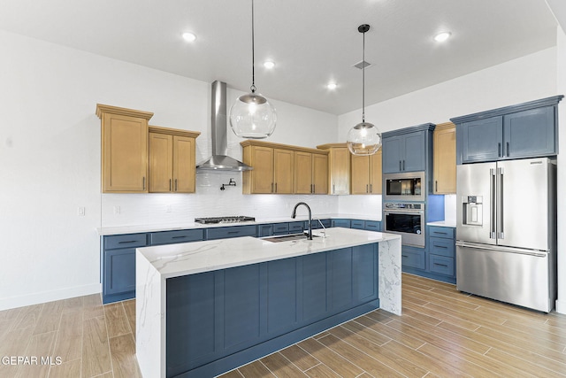 kitchen featuring appliances with stainless steel finishes, a kitchen island with sink, sink, pendant lighting, and wall chimney exhaust hood