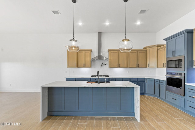 kitchen featuring appliances with stainless steel finishes, wall chimney exhaust hood, decorative light fixtures, sink, and tasteful backsplash