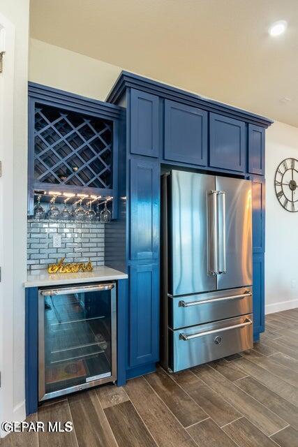 bar with blue cabinets, high end refrigerator, and beverage cooler