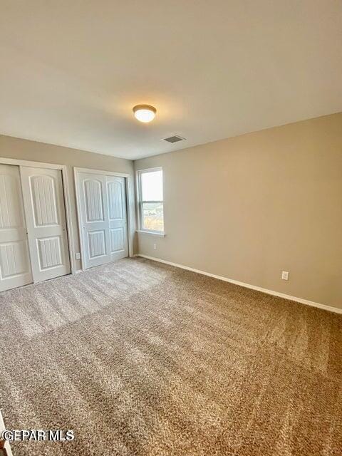 unfurnished bedroom featuring carpet flooring and two closets