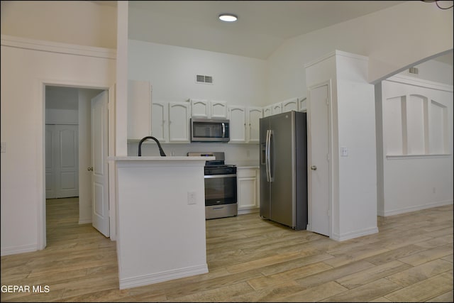 kitchen with stainless steel appliances, sink, white cabinetry, kitchen peninsula, and light hardwood / wood-style flooring