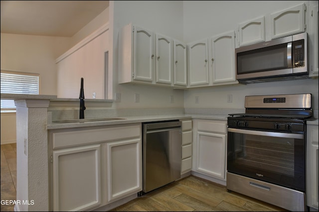 kitchen featuring kitchen peninsula, light wood-type flooring, white cabinets, appliances with stainless steel finishes, and sink