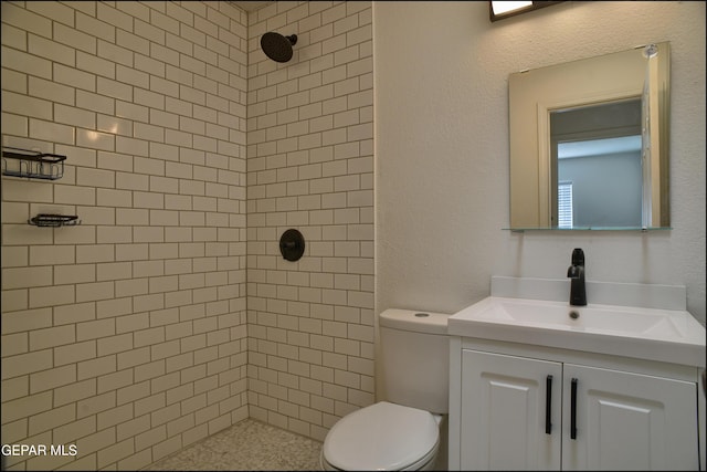 bathroom featuring toilet, a tile shower, and vanity