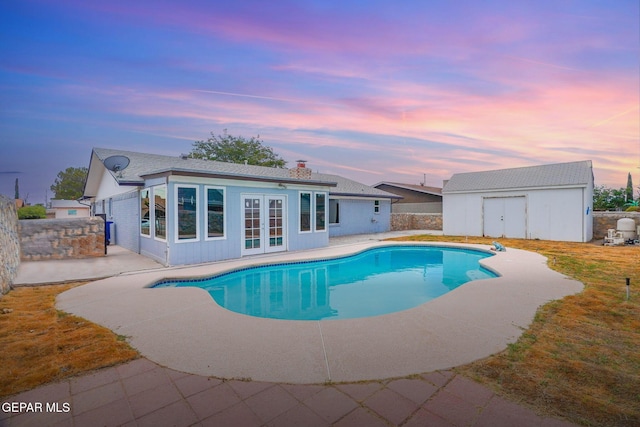 pool at dusk with a patio and an outbuilding