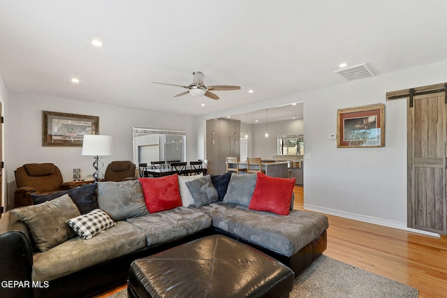 living room with ceiling fan, a barn door, and wood-type flooring