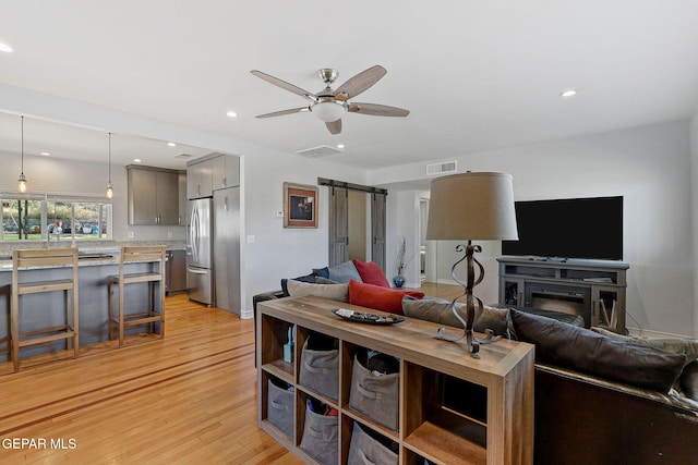 living room featuring ceiling fan, light hardwood / wood-style floors, and a barn door