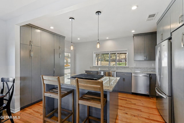 kitchen featuring stainless steel appliances, hanging light fixtures, light stone counters, sink, and light hardwood / wood-style flooring