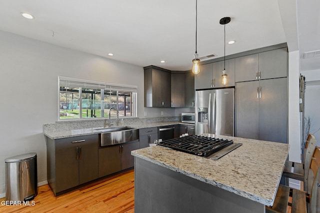 kitchen featuring stainless steel appliances, a center island, light stone counters, and hanging light fixtures