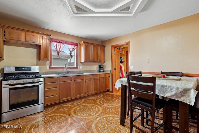 kitchen featuring sink, stainless steel gas stove, light tile patterned flooring, and a textured ceiling