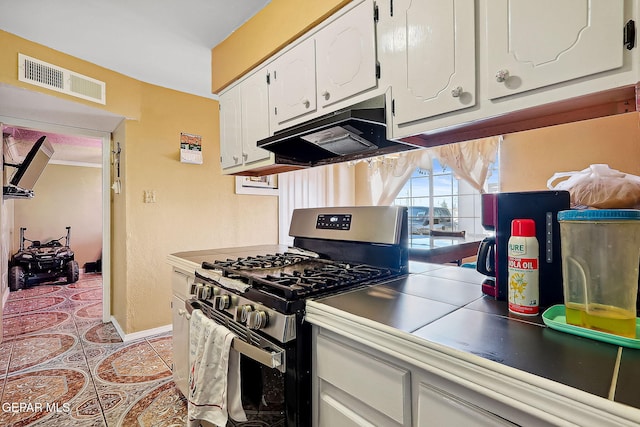 kitchen with stainless steel gas range, light tile patterned flooring, and white cabinetry