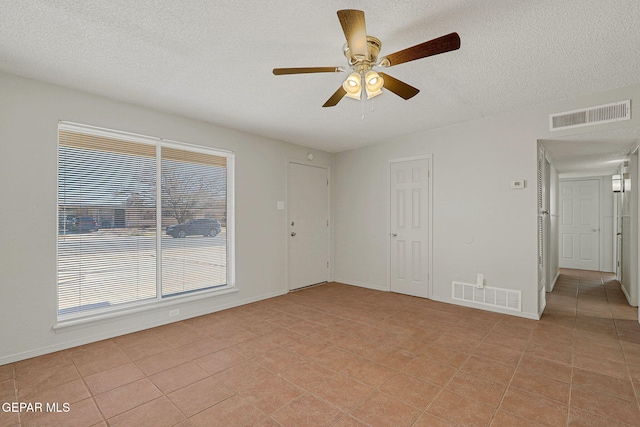 tiled empty room with ceiling fan, a wealth of natural light, and a textured ceiling