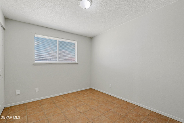 empty room with a textured ceiling and light tile patterned floors