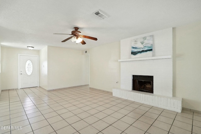 unfurnished living room with ceiling fan, light tile patterned floors, a brick fireplace, and a textured ceiling