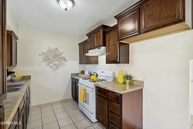 kitchen with light tile patterned flooring, white gas stove, dark brown cabinetry, and sink