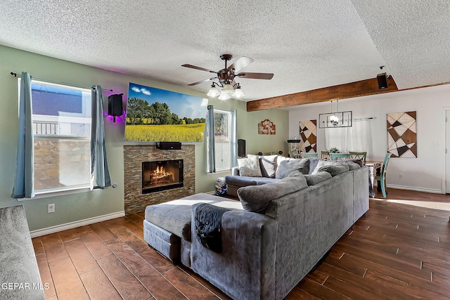 living room with a textured ceiling, ceiling fan, beamed ceiling, and a stone fireplace