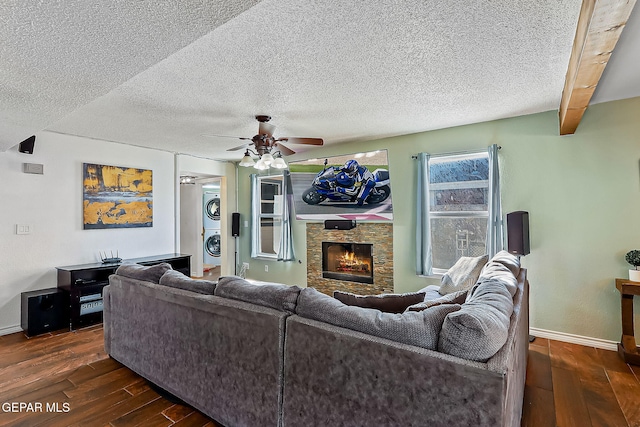 living room with a fireplace, a textured ceiling, ceiling fan, stacked washer and dryer, and dark hardwood / wood-style flooring