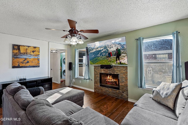 living room with dark wood-type flooring, a textured ceiling, stacked washer and dryer, ceiling fan, and a stone fireplace