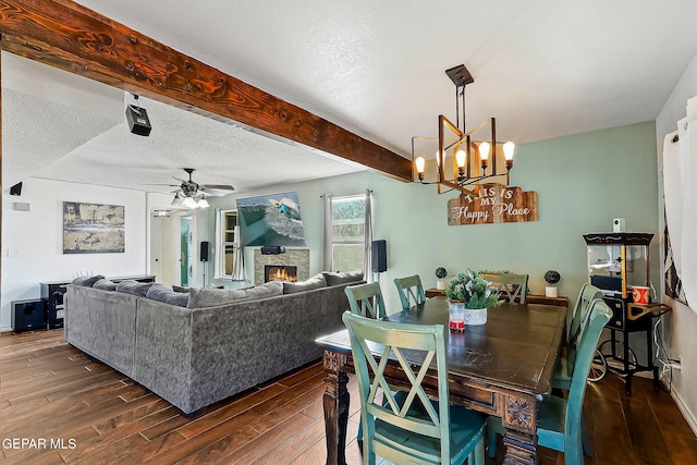 dining space featuring a textured ceiling, dark hardwood / wood-style flooring, ceiling fan with notable chandelier, a fireplace, and beamed ceiling