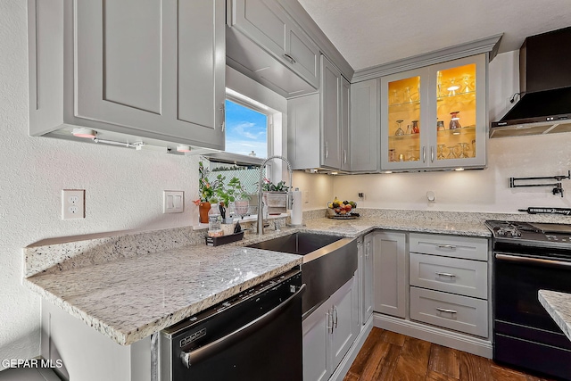 kitchen featuring light stone countertops, dark hardwood / wood-style floors, wall chimney range hood, black appliances, and gray cabinetry