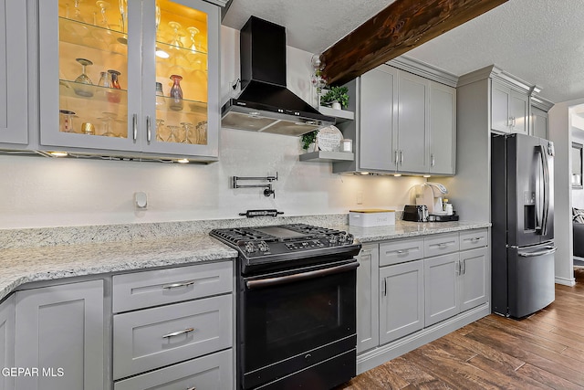 kitchen with black gas range, beamed ceiling, dark wood-type flooring, stainless steel refrigerator with ice dispenser, and wall chimney range hood