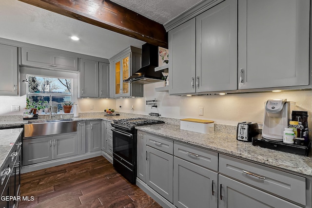 kitchen featuring black gas range oven, gray cabinets, light stone counters, and wall chimney exhaust hood