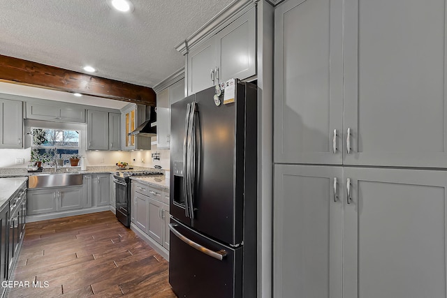 kitchen featuring light stone countertops, black fridge with ice dispenser, stainless steel range with gas cooktop, beamed ceiling, and sink