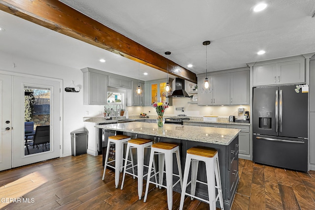 kitchen with gray cabinets, a center island, light stone countertops, stainless steel refrigerator with ice dispenser, and wall chimney range hood