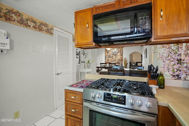 kitchen with a textured ceiling, light tile patterned flooring, and stainless steel range with gas cooktop