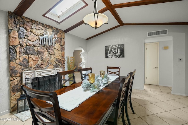 dining space featuring a fireplace, light tile patterned flooring, and vaulted ceiling with skylight