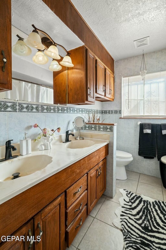 bathroom featuring tile patterned flooring, toilet, vanity, tile walls, and a textured ceiling