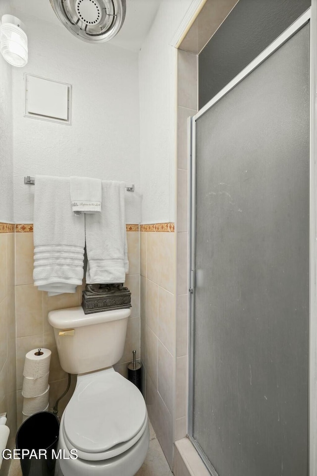 bathroom featuring toilet, an enclosed shower, and tile walls