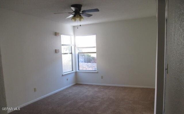 empty room with ceiling fan, a healthy amount of sunlight, and dark carpet