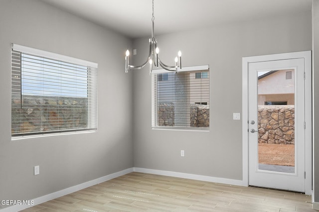 unfurnished dining area with light wood-style floors, baseboards, and an inviting chandelier