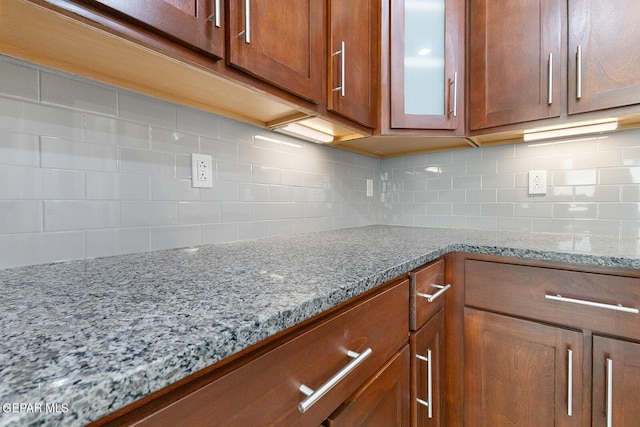 kitchen featuring tasteful backsplash, brown cabinetry, glass insert cabinets, and light stone countertops