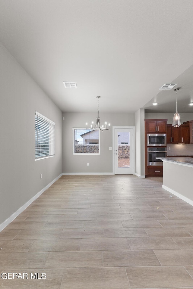 unfurnished living room with visible vents, a notable chandelier, and baseboards