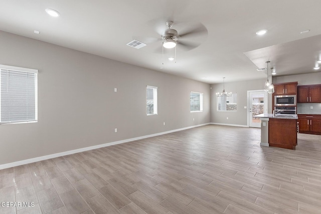 kitchen with open floor plan, oven, a kitchen island with sink, built in microwave, and pendant lighting