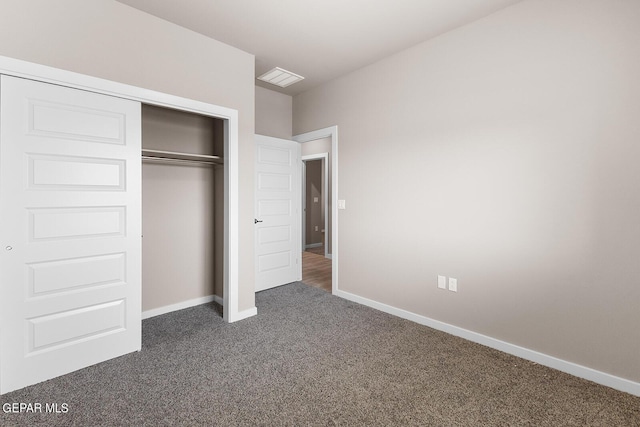 unfurnished bedroom featuring a closet, visible vents, dark carpet, and baseboards