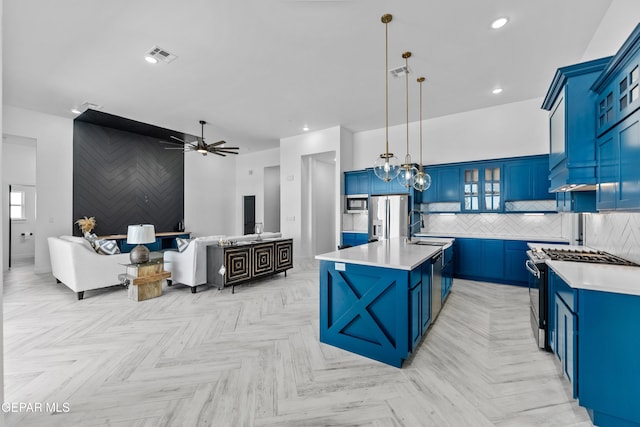 kitchen featuring stainless steel appliances, blue cabinets, pendant lighting, and an island with sink