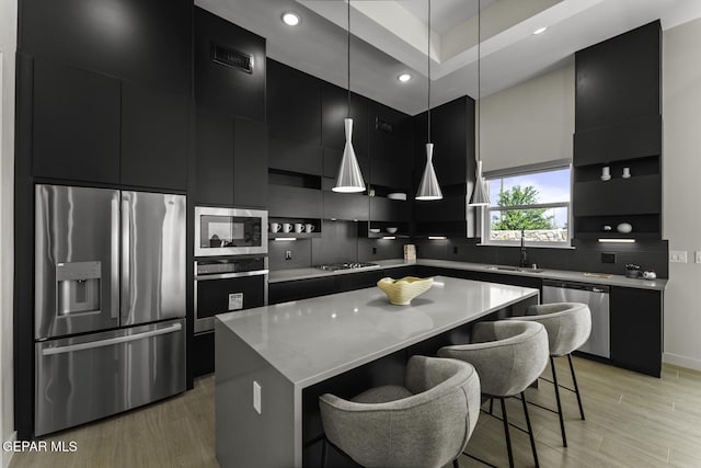 12869 Kingsbury Ave, Horizon City, TX 79928 - kitchen with appliances with stainless steel finishes, dark cabinets, a kitchen breakfast bar, light wood-style flooring, and modern cabinets