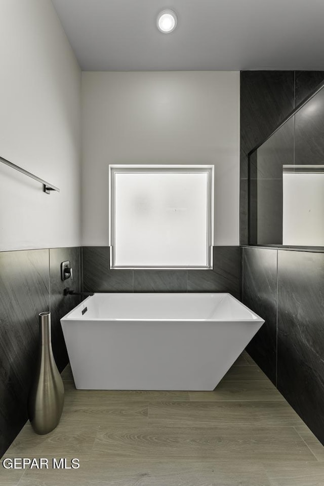 12869 Kingsbury Ave, Horizon City, TX 79928 - bathroom featuring tile walls, a soaking tub, wood finished floors, and a wainscoted wall