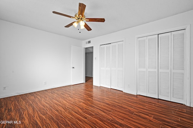 unfurnished bedroom featuring ceiling fan, two closets, and dark wood-type flooring