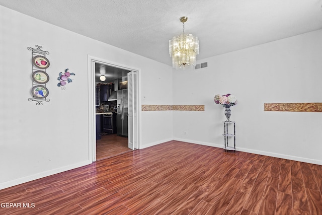 spare room with dark hardwood / wood-style floors, an inviting chandelier, and a textured ceiling